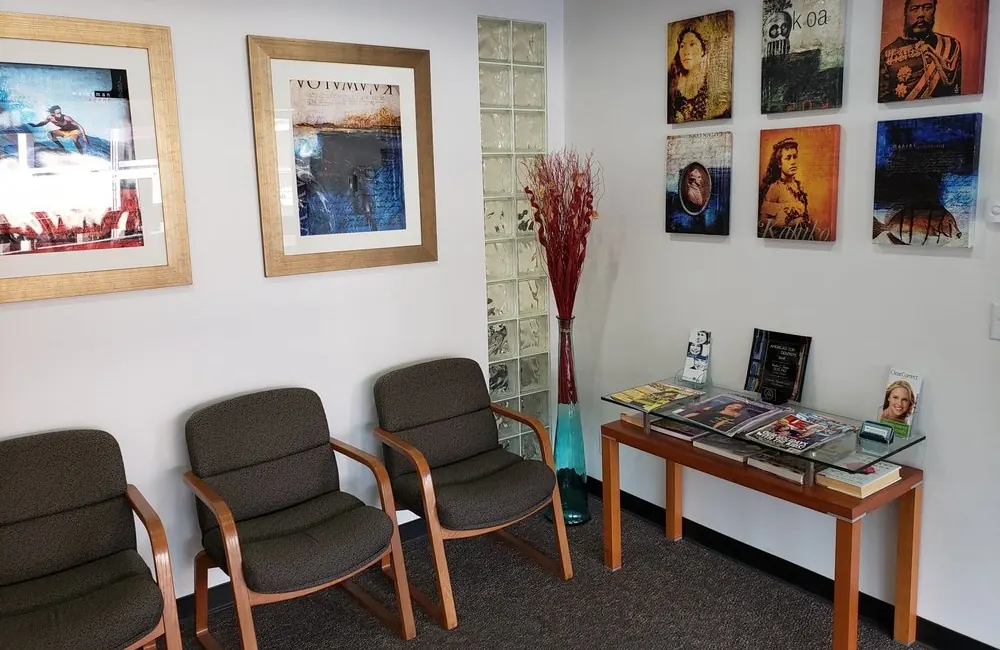 Upholstered chairs and framed Hawaiian art in the Hawaii Cosmetic Dental waiting room.